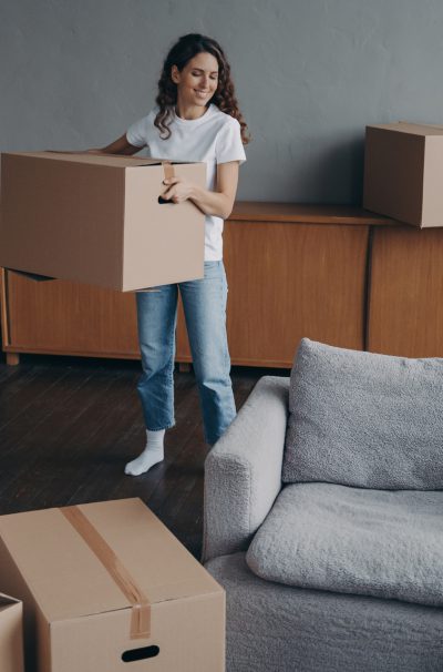 Hispanic girl is holding box and leaving apartment. Happy young woman relocates alone. Single lady moves. Real estate purchase, mortgage, delivery service ordering concept.